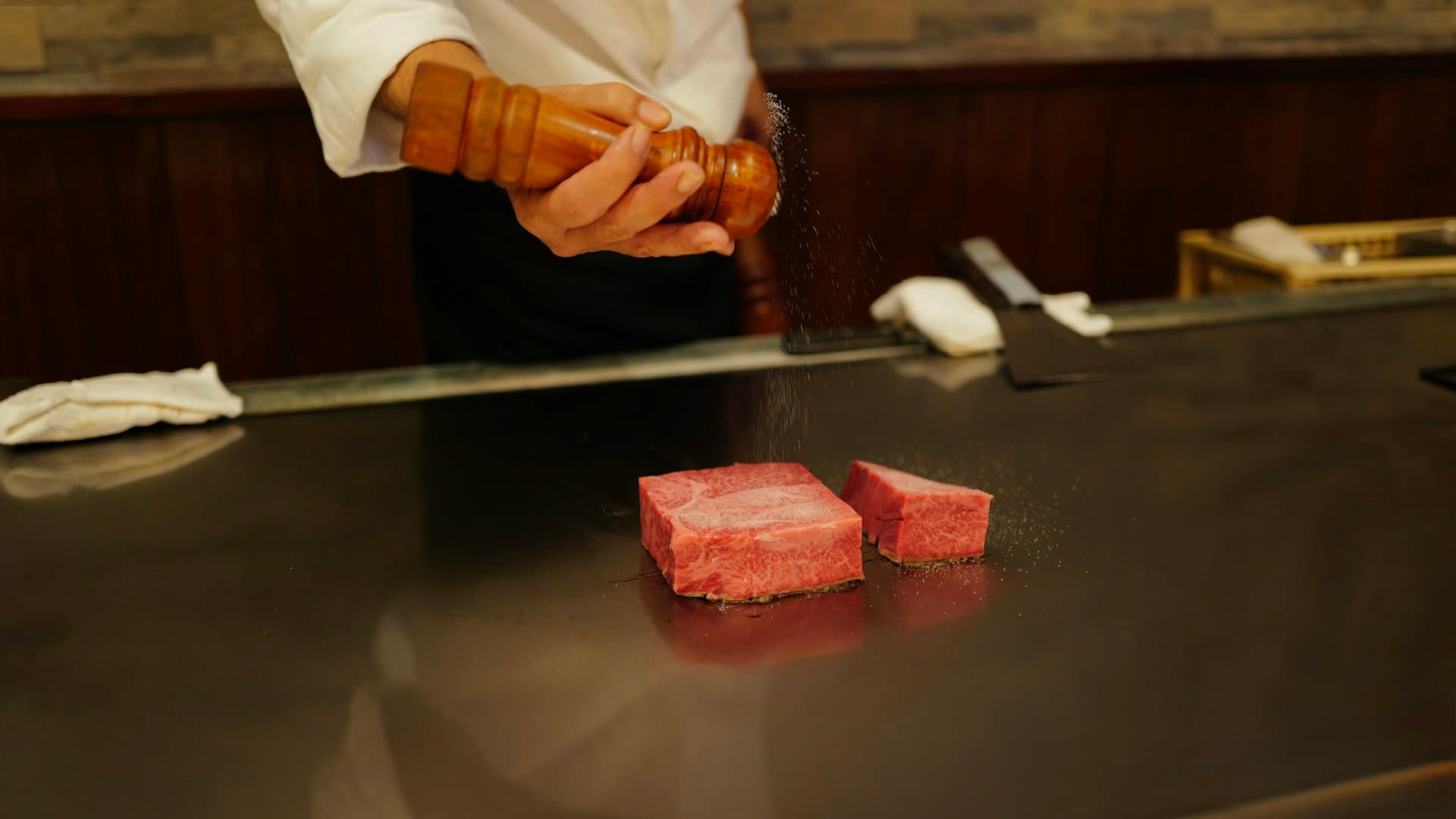 A chef sprinkling coarse sea salt over a raw piece of high-quality beef.