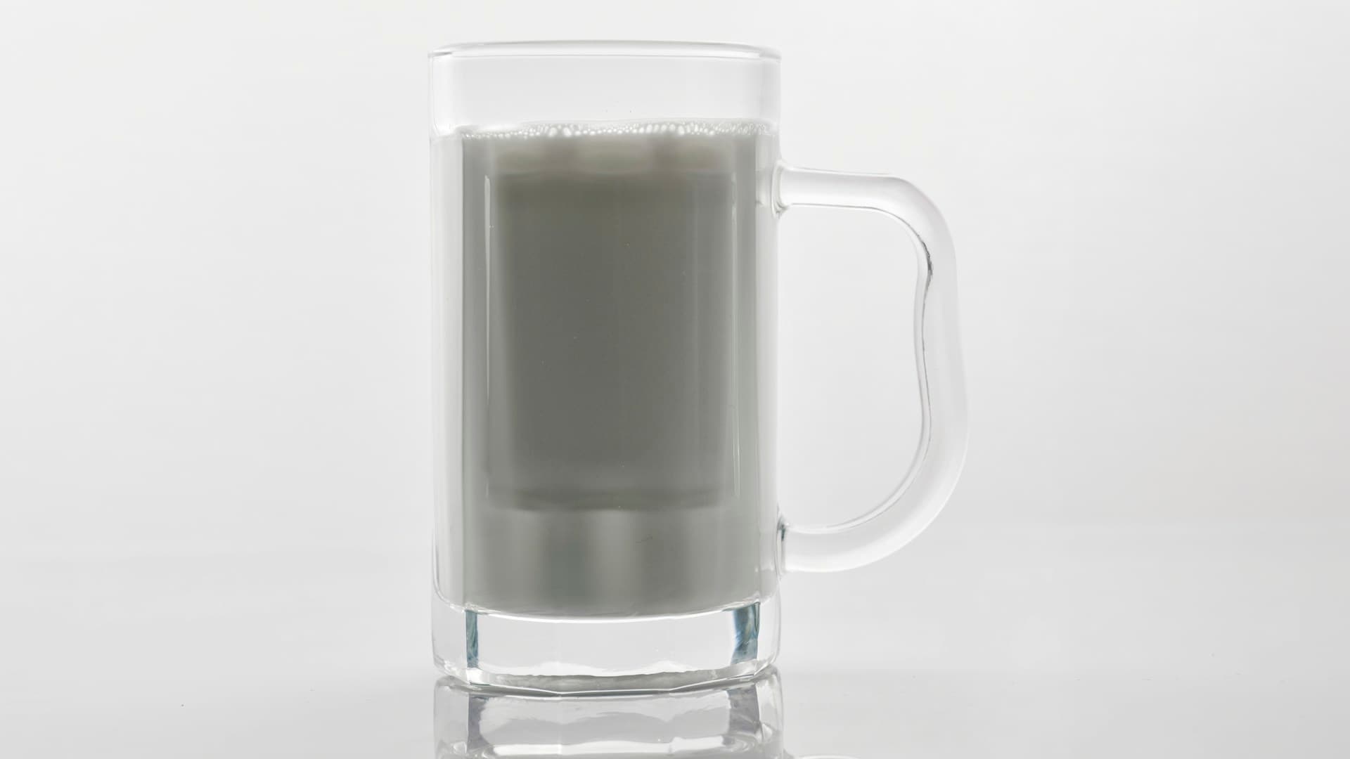 A clean, minimalist shot of a carnivore protein shake in a glass next to a scoop of unflavoured beef protein isolate powder.
