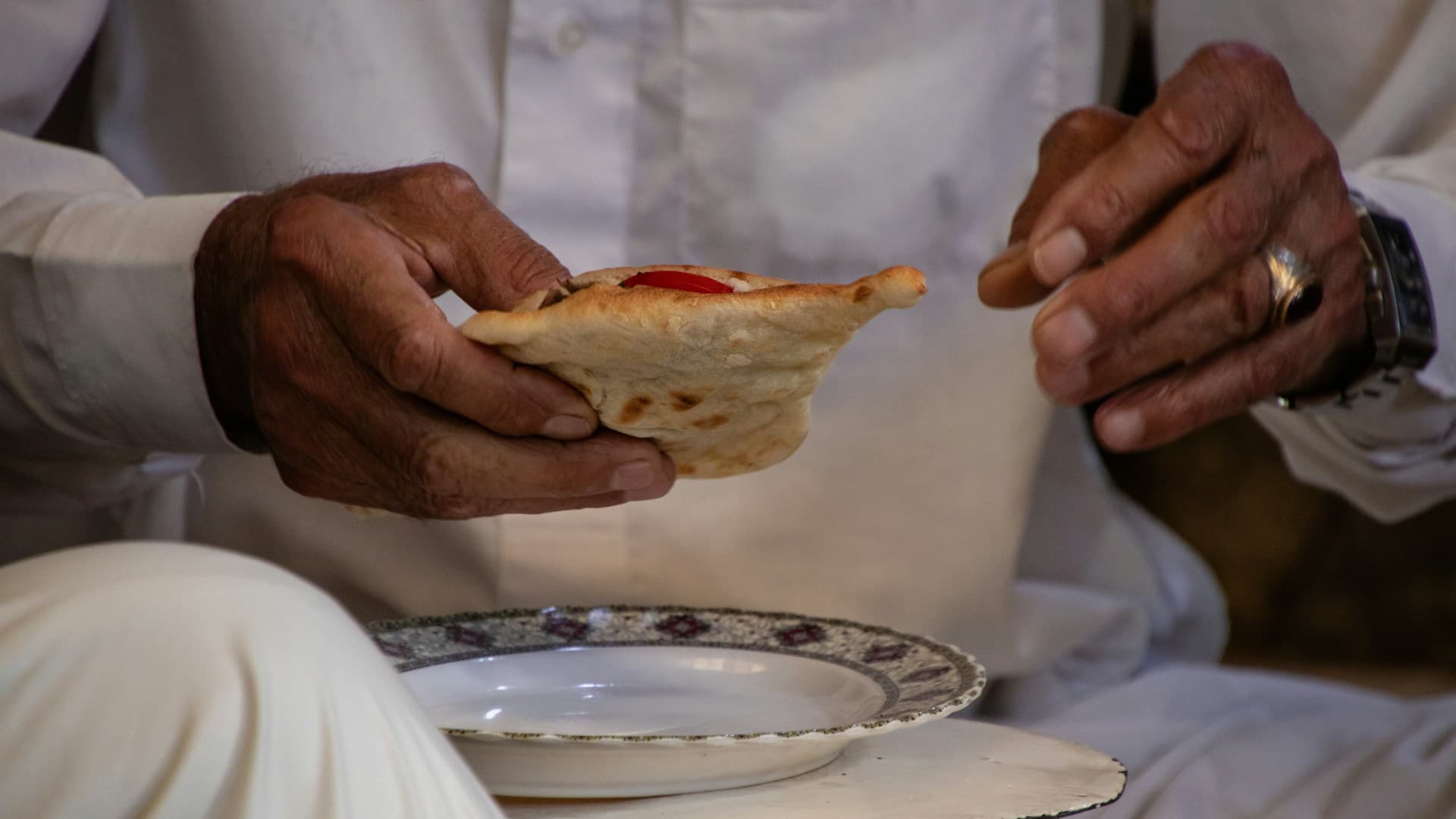 A close-up of a person assembling a Mediterranean taco, layering fresh salsa on top of grilled chicken in a pita.