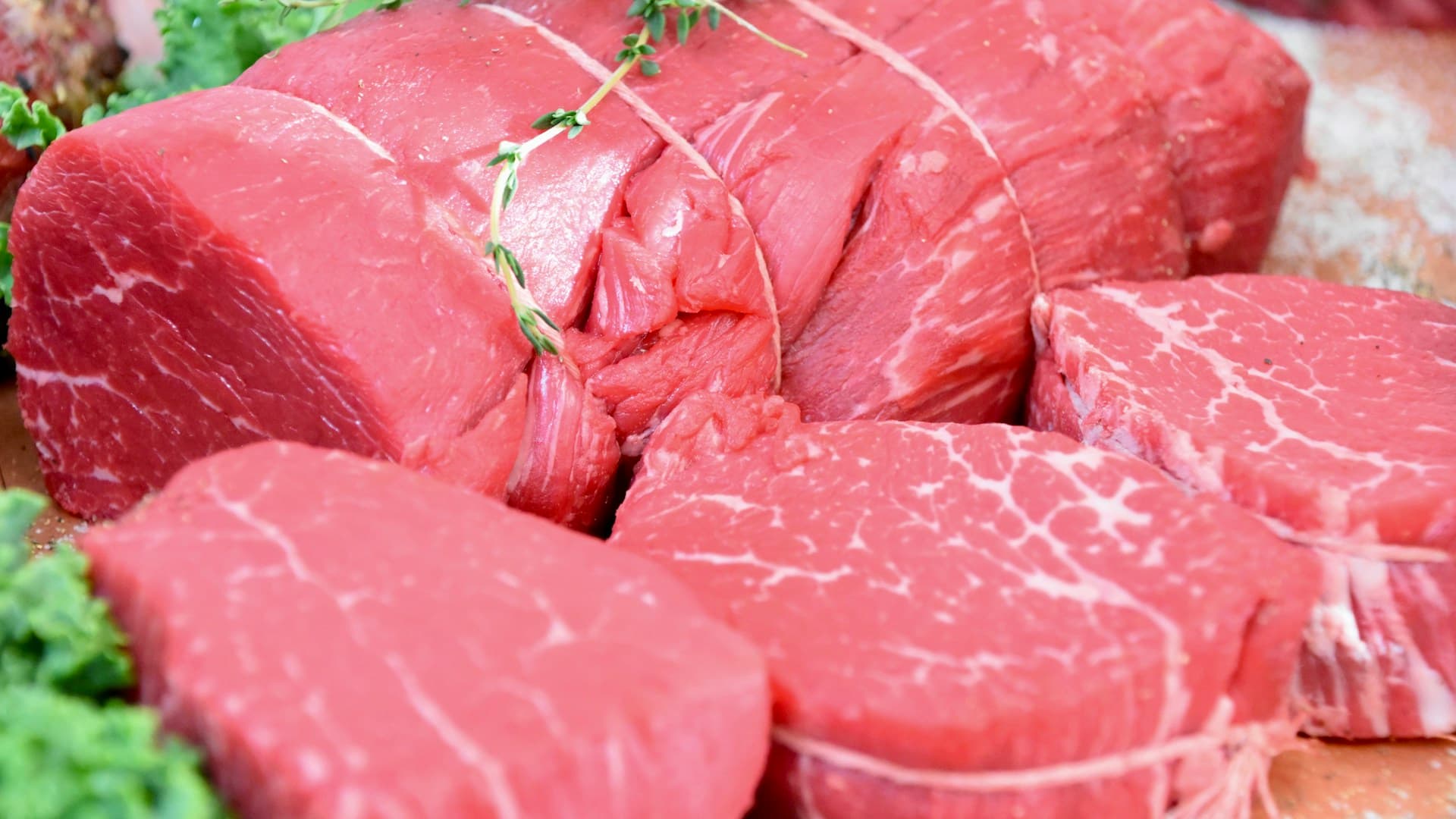 A close-up of a variety of fresh cuts of raw meat, including steaks and ground beef, laid out on a butcher's block.