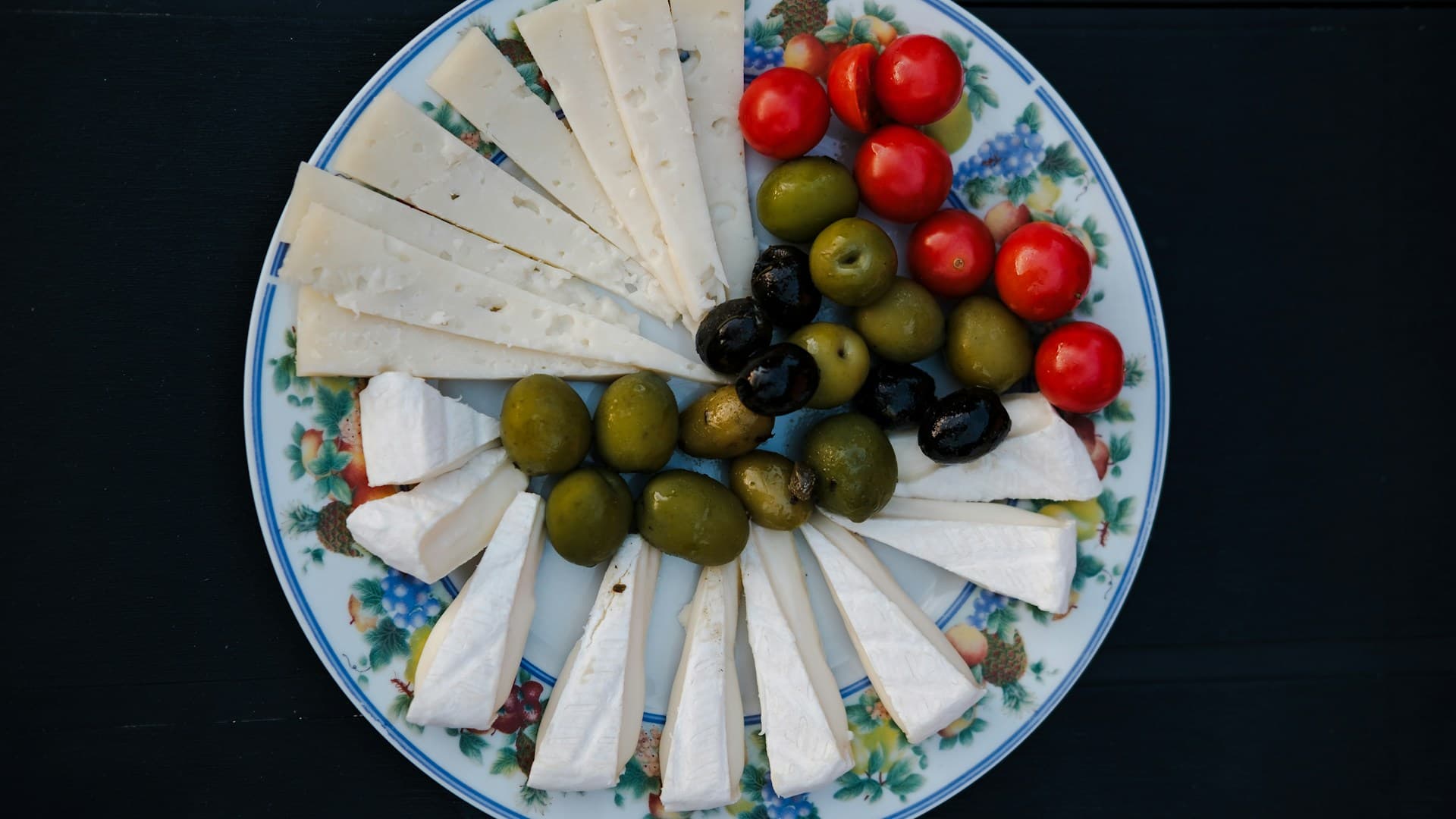 A display of key Mediterranean ingredients including a bottle of extra virgin olive oil, fresh herbs, feta cheese, and colourful vegetables.