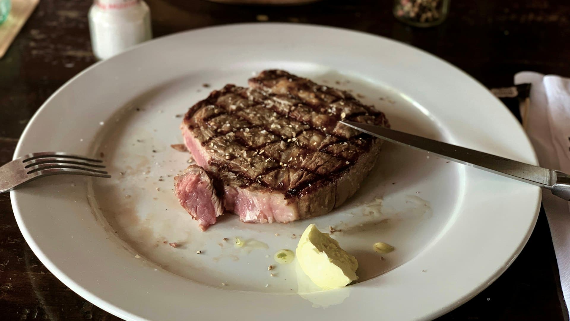 A flat lay of various carnivore diet foods, including a large ribeye steak, salmon fillets, eggs, and butter on a wooden board.