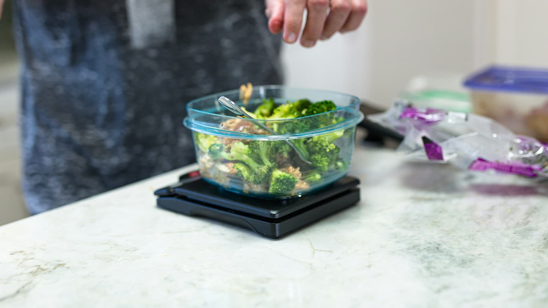 A high-speed blender surrounded by fresh smoothie ingredients such as spinach, mixed berries, an avocado, and a bowl of almonds on a kitchen counter.