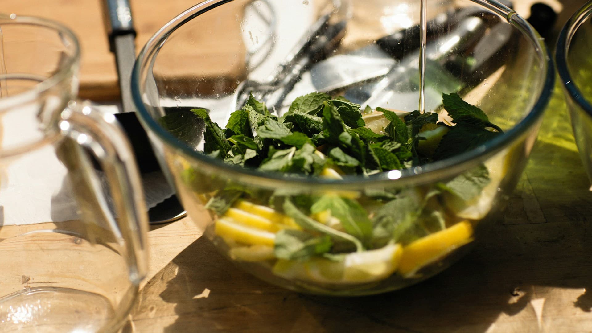 A person is whisking a simple vinaigrette of olive oil and lemon juice in a small glass bowl to dress the cucumber salad.